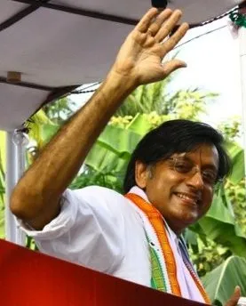 Politician Shashi Taroor with his hand raised, addressing the mass.